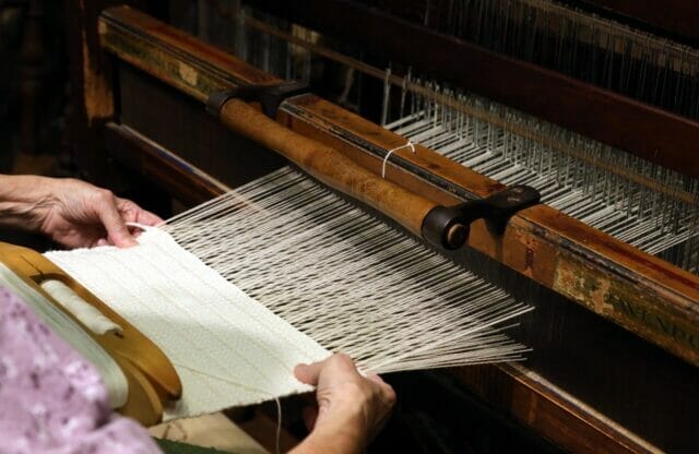 person feeds slivers into spinning device turning fibers into yarn