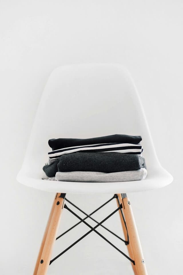A stack of clothes on a white modern chair, image by Sarah Dorweiler from Unsplash