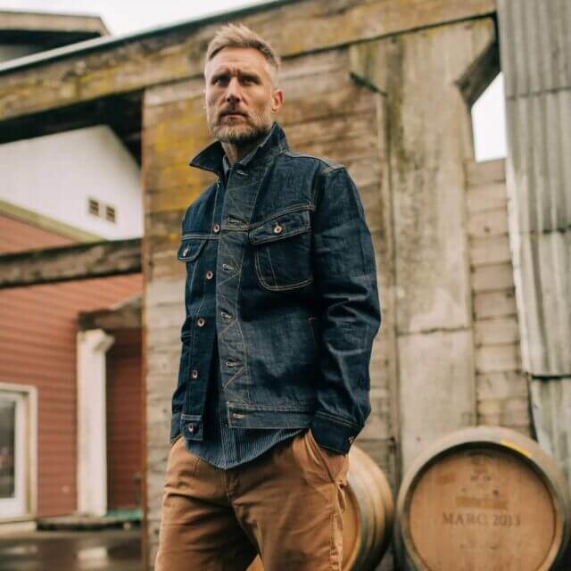 A model posing and showcasing Taylor Stitch's heavy duty jacket in front of an industrial building