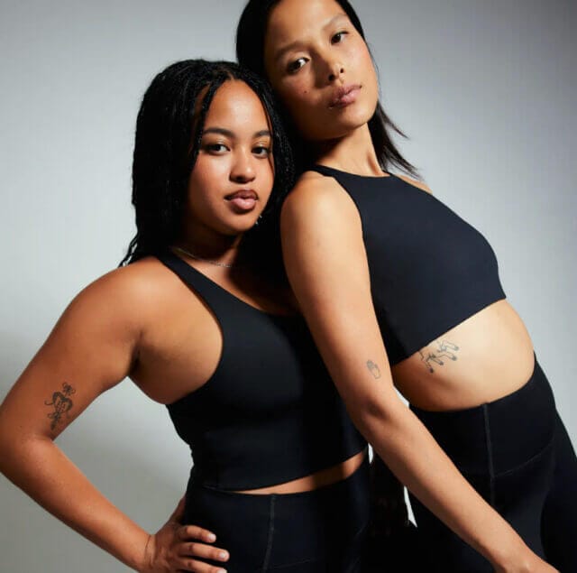 Two girls both wearing black crop tops and leggings stand together