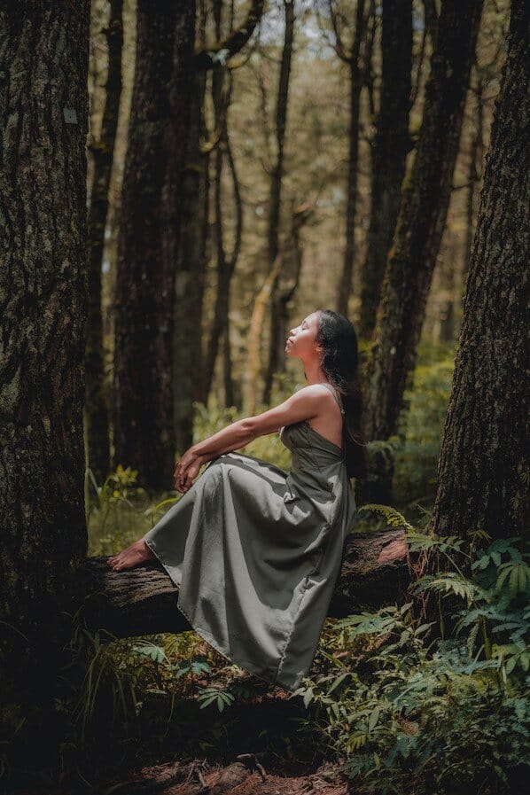 Woman wearing long green dress sat on a fallen branch in the jungle