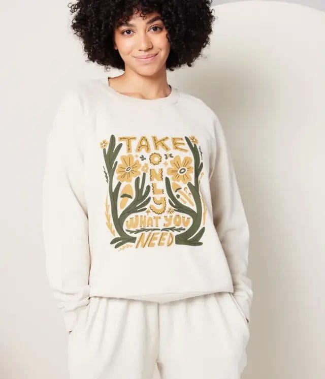 Woman with curly hair wears white tracksuit with message reading 'take only what you need'