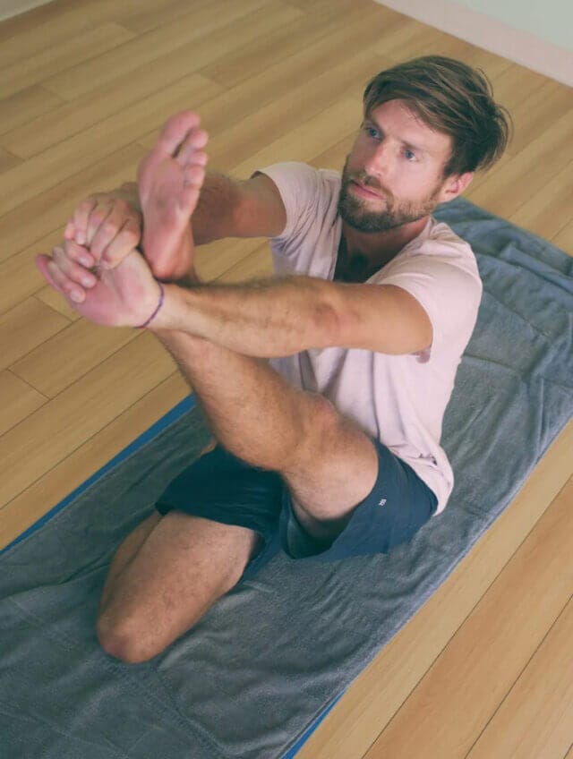 Man doing yoga on a mat inside wearing a pink shirt and blue shorts