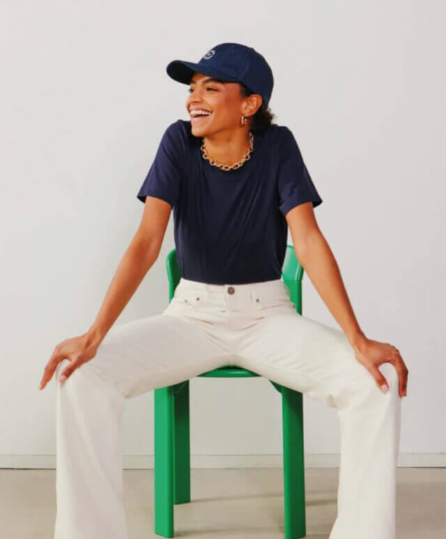 Person wearing white trousers and a navy hat and top sits on a bright green chair