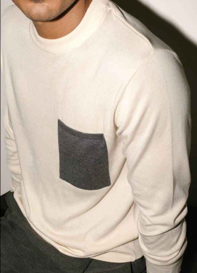 Man wearing a white jumper with a grey pocket, with his face not visible 
