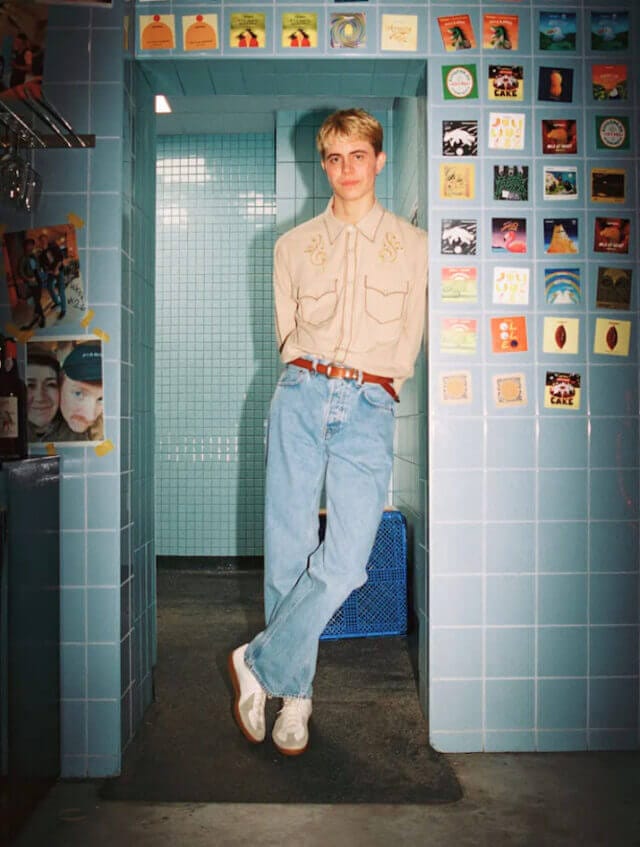 Man wearing a cowboy style shirt and jeans stands in a tiled doorway