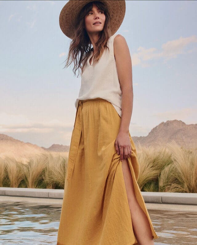 Woman with sun hat and yellow skirt stands with a desert in the background