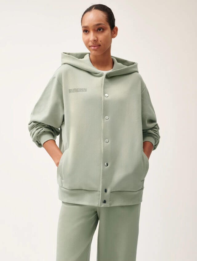 Woman wearing sage green trousers and buttoned hoodie looks to left