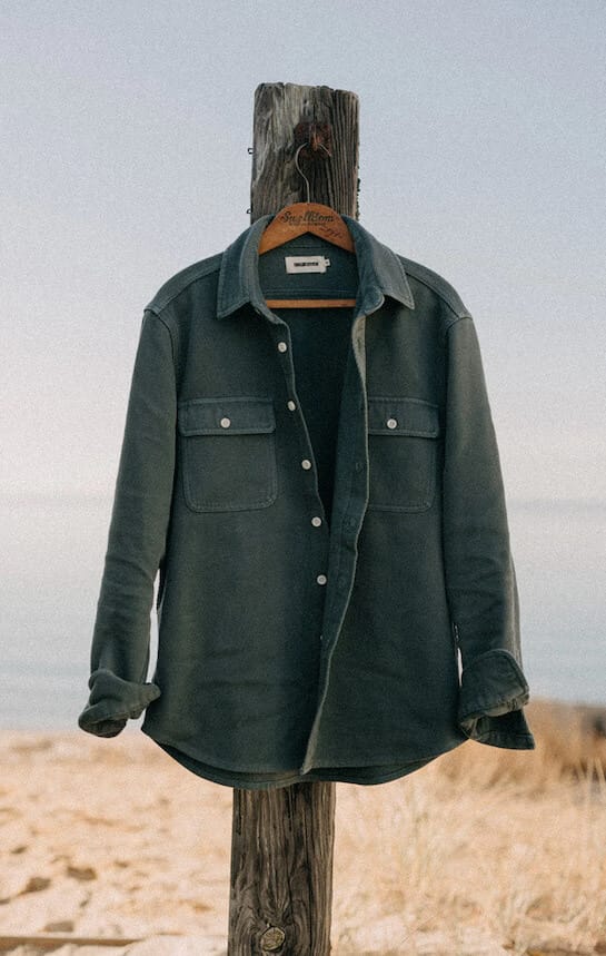 A grey jacket is on a coat hanger that is hanging on a piece of wood, with the sea in the background
