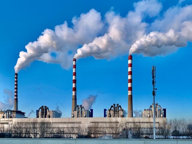 An image of a huge factory polluting the air. Image by Andreas Felske from Unsplash
