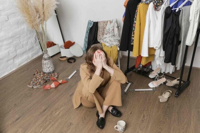 Woman sitting on the floor with nothing to wear yet a wardrobe full of clothes
