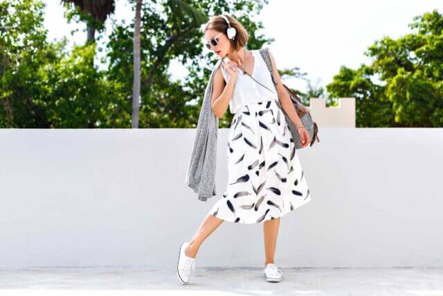 woman with headphones and printed skirt standing outside