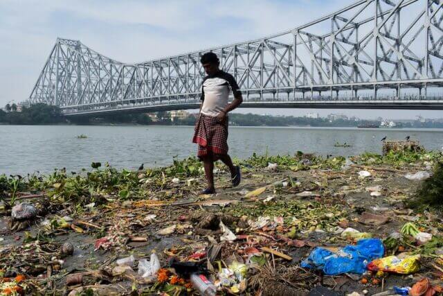 Man walking a long a river littered with different types of pollution