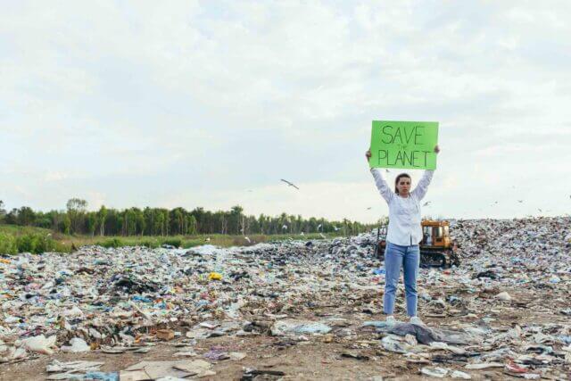 woman in landfill holding sign that says save the planet