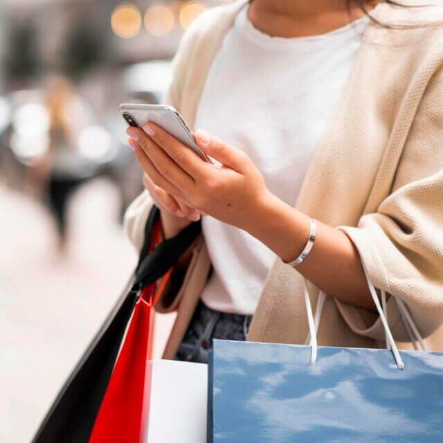Shopper looking at her phone whilst holding lots of shopping bags 