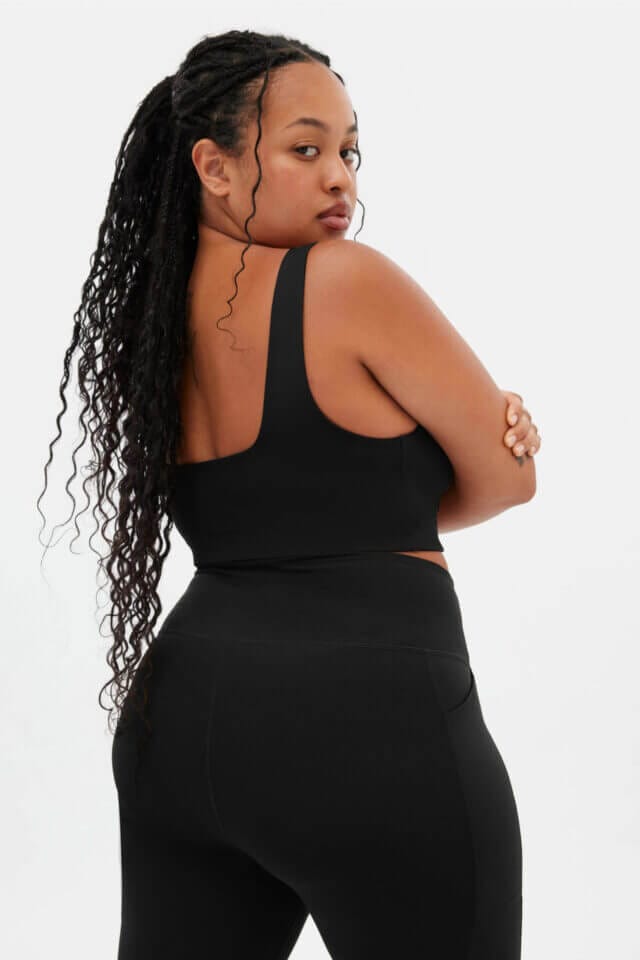 A plus-size model wearing a black cropped top and a leggings from Girlfriend Collective.