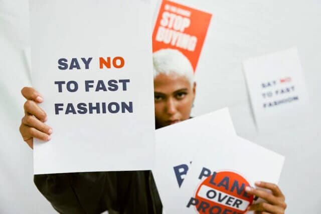activist holds sign that says "say no to fast fashion"