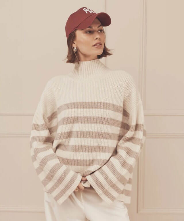 A female model wearing a red cap with a stripe soft winter jumper from NAADAM.