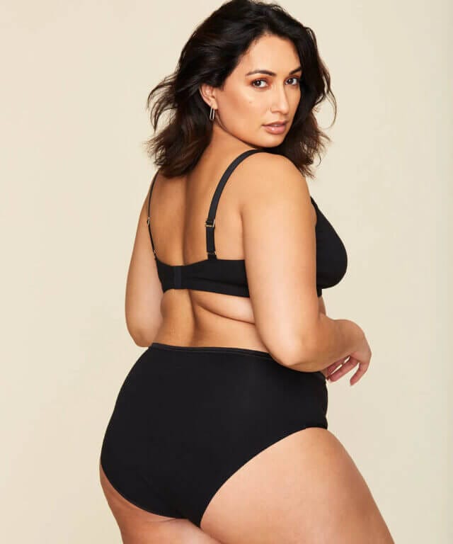 A plus-size model wearing a black bra and undies from Subset.