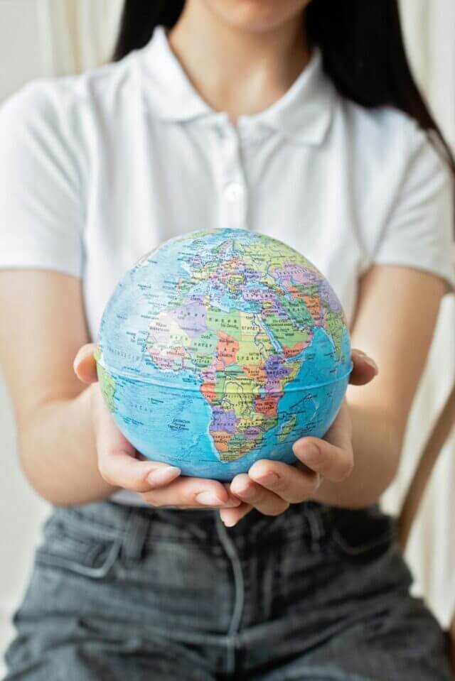 A woman wearing a denim and a white polo has a globe in her hands.