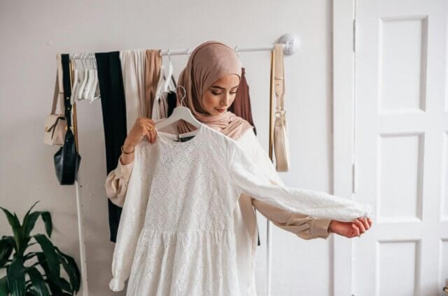 Woman in hijab holding a white top in front of her to see how it fits. First image for blog on eco-friendly petite and tall fashion
