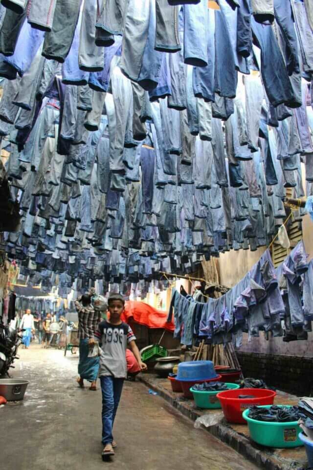 A child walks into a street full of denim hanging to dry out.