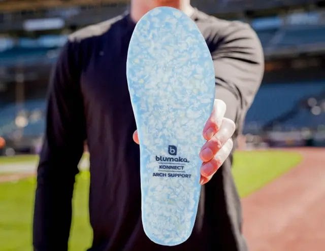 athlete in a sports stadium holding the blumaka insoles in front of the camera to show the details