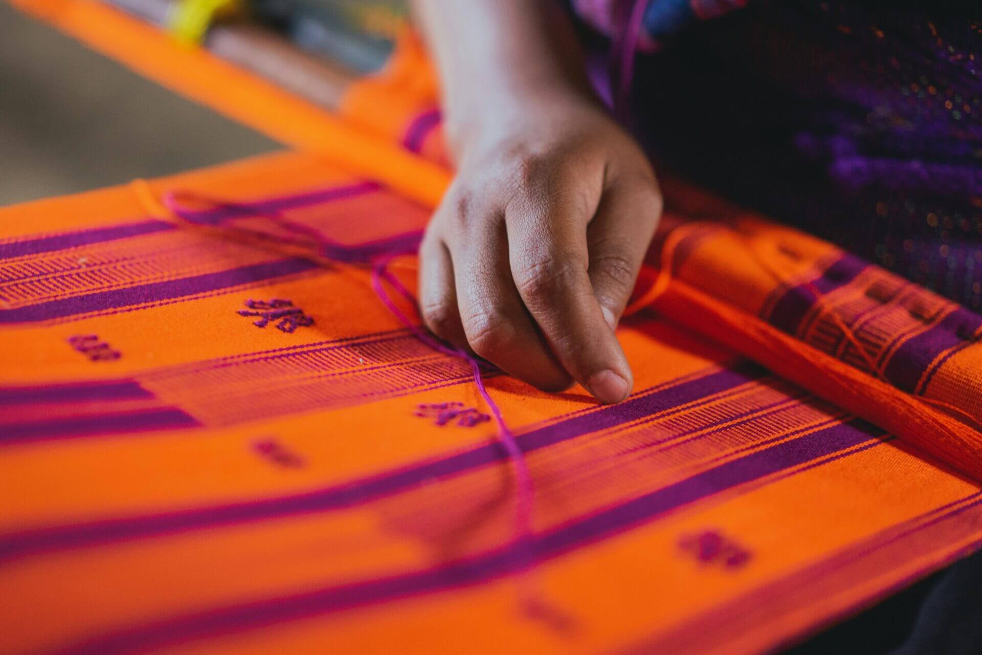 A close-up of a hand weaving a colorful pattern